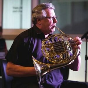 A musician playing a French horn on stage, focused and engaged in the performance.